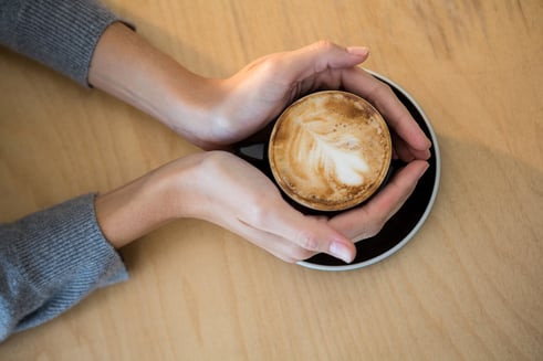 Woman holding cup of coffee on table in cafeteria